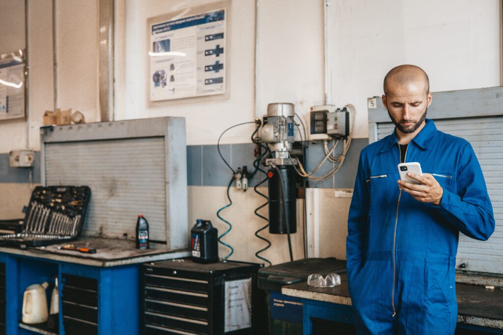 Mann in Werkstatt schaut auf sein Handy und nutzt es zur Digitalisierung des Geschäftsprozesses